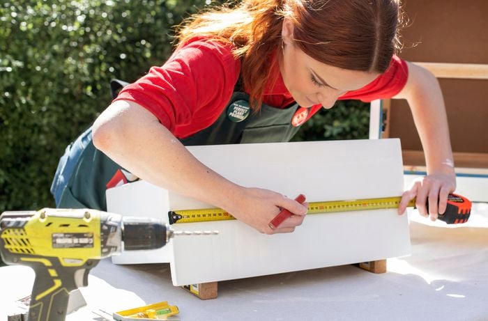Woman using a tape measure and pencil to mark the front of a drawer