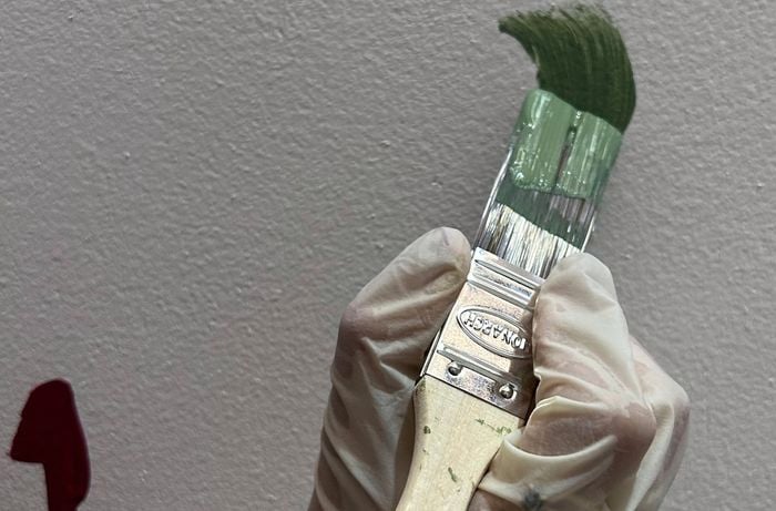A gloved hand paints the terrazzo shapes on the wall