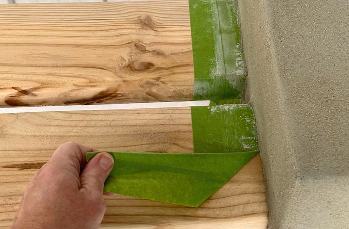 A person peels painter’s tape off timber slats]