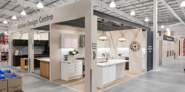Kitchen Design Centre display inside a Bunnings warehouse, featuring multiple kitchen layouts with cabinetry, benchtops, lighting, and appliances in a showroom setting.
