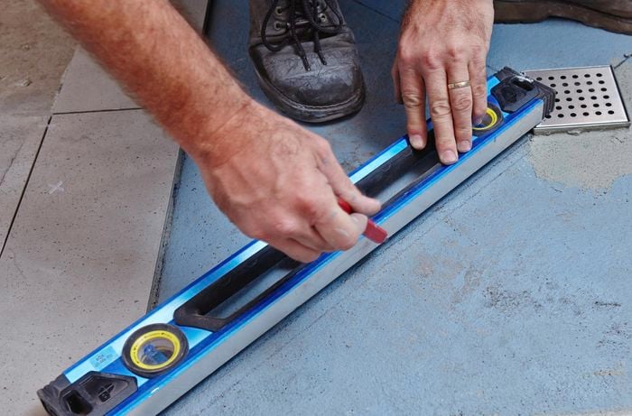 A person marking a diagonal line on a shower base using a spirit level