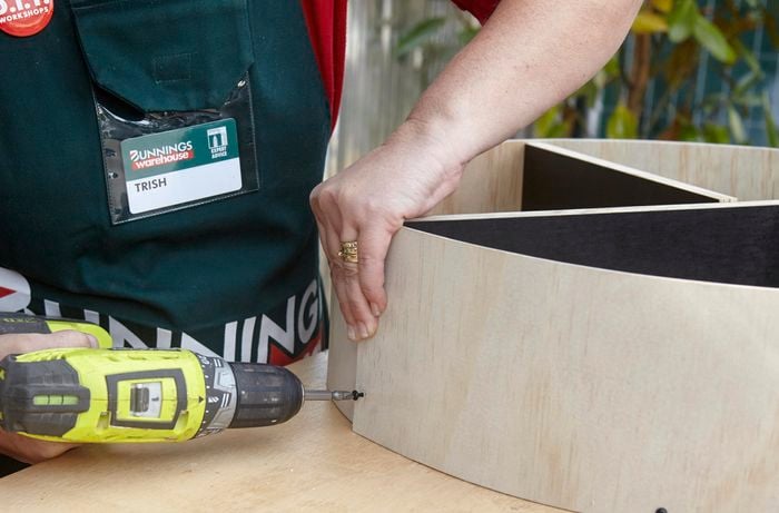 A person screwing into a strip of plywood curved around a circular plywood base