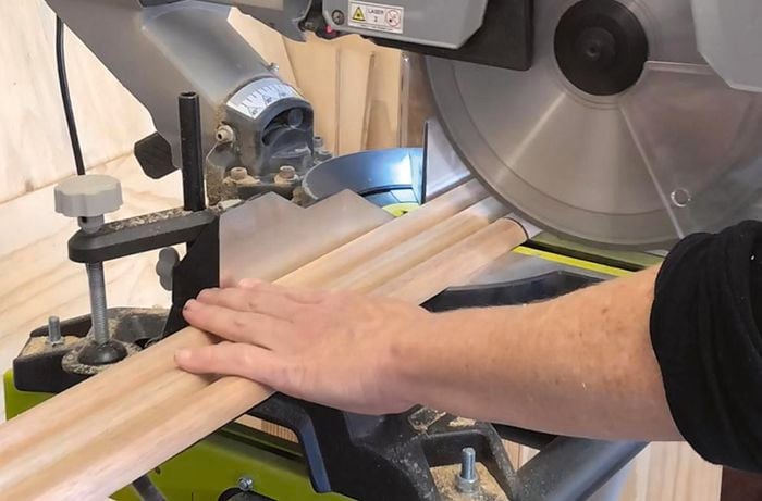 A person cutting three lengths of thick dowel with a drop saw