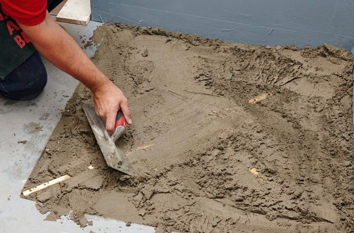 A person using a flat trowel to spread screed across a shower base