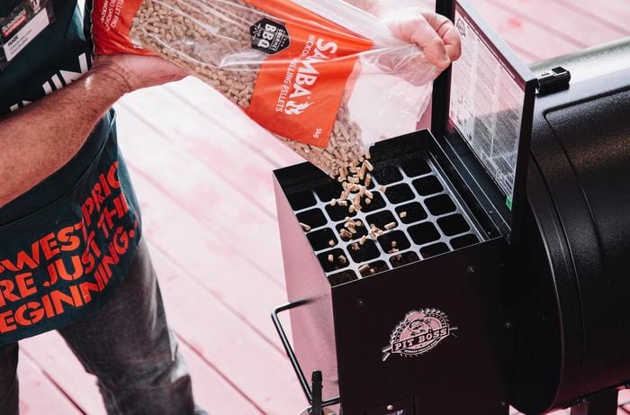 Person pouring pellets into the hopper of a pellet smoker