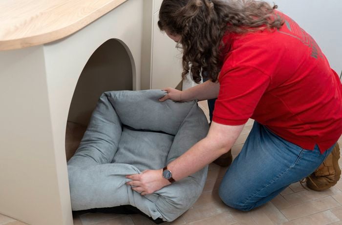 A Bunnings Team Member is placing a soft grey pet bed into a nook under the built-in cabinetry.