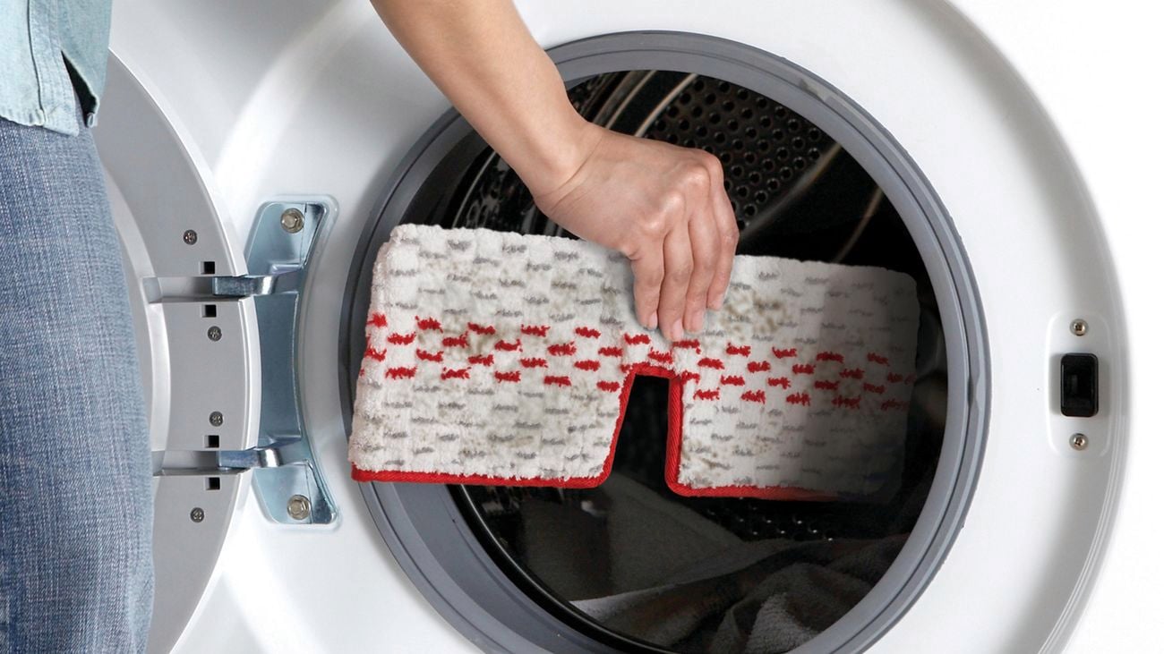 A woman loading a Vileda spray mop head into a washing machine