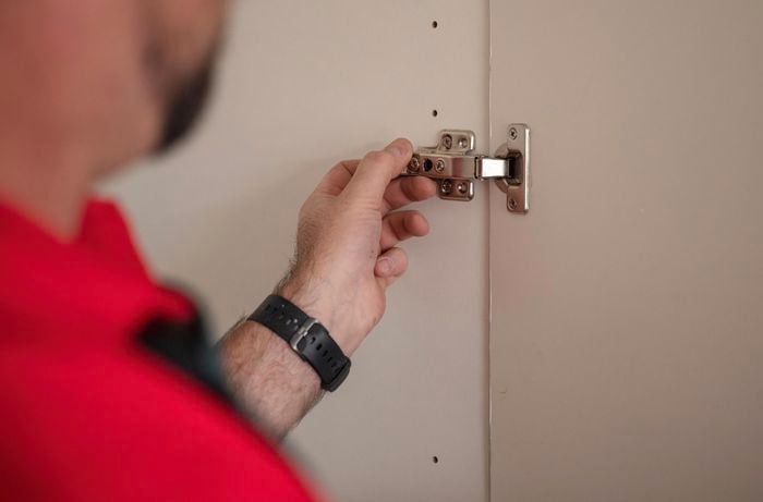 A person uninstalling cupboard door hinges.