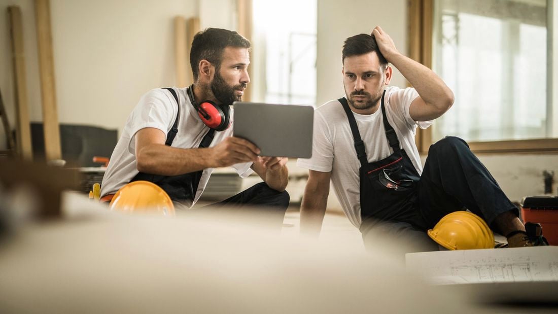 Two tradies sitting down at a worksite and looking at an iPad.