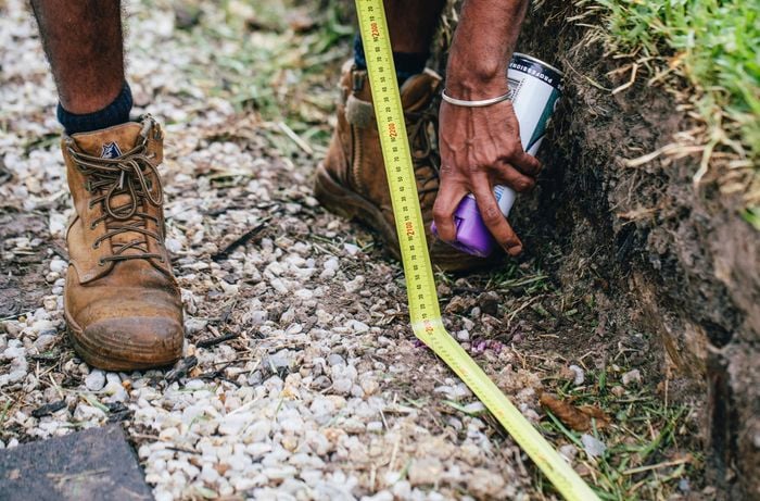 Marking out the dimensions of a retaining wall with a tape measure and a marker paint can