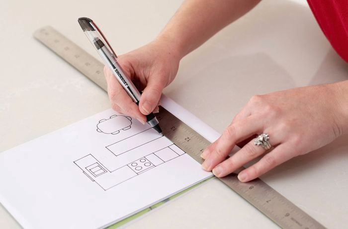 A person is making a sketch of a kitchen layout on paper using a ruler and pen