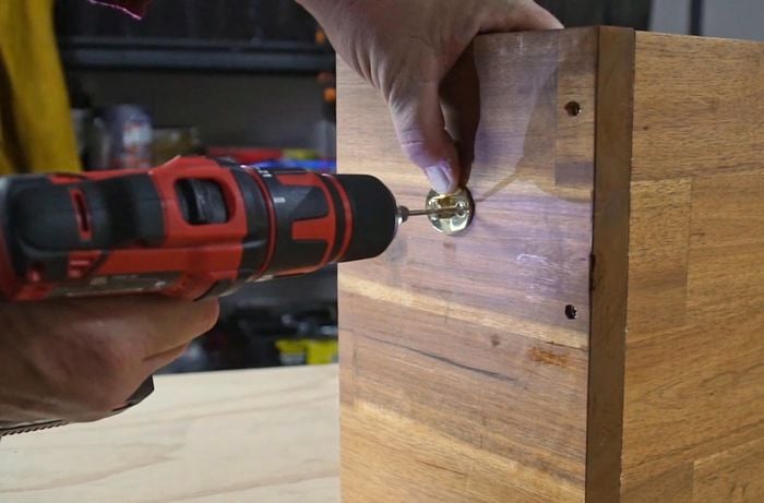 Hands using a power drill to drill a pilot hole through brass handles into timber