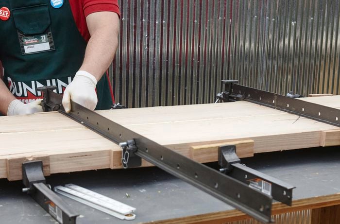 A person clamping two lengths of timber using bench clamps