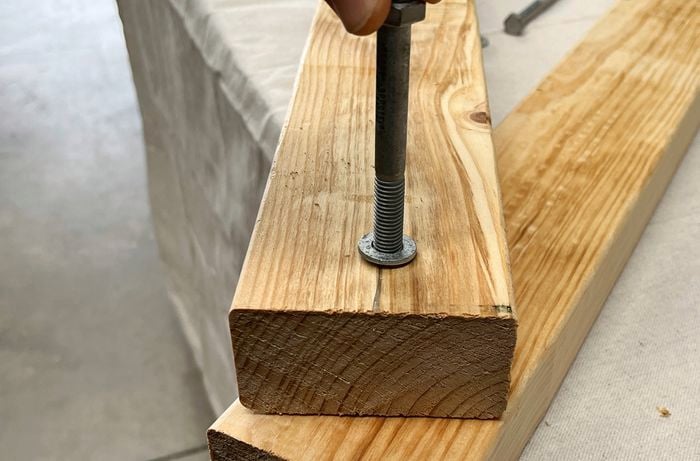 A bolt being driven into two pieces of timber stacked in a V shape.