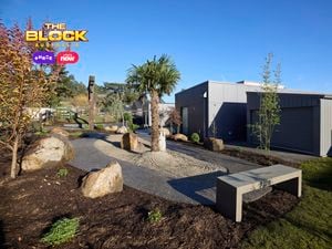The front area of a house with a bench seat, rocks, grassed area and trees in it.