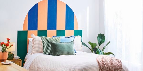 A D.I.Y. bed headboard in green, blue and apricot behind a double bed piled with pillows