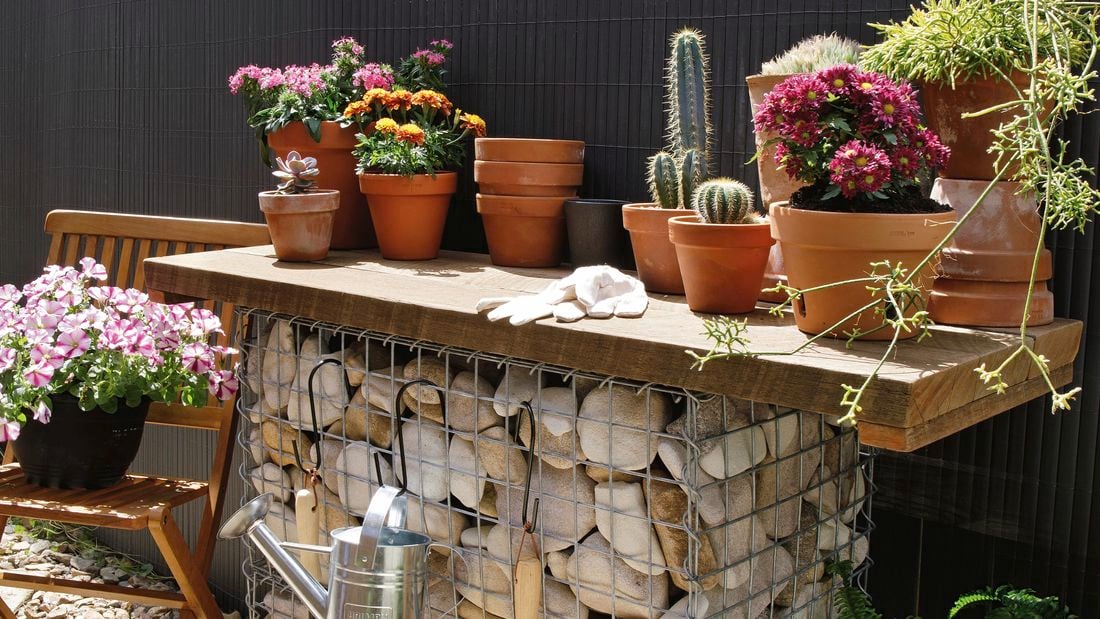 A completed gambion potting bench with trowel, stainless steel watering can and several potted succulents on top