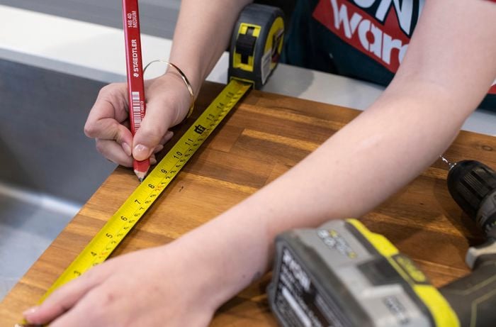 A length of timber being measured and marked for drilling with a tape measure and pencil