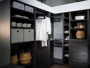 Walk in wardrobe with drawers, shelves, clothes hanging on coat hangers and shoes.
