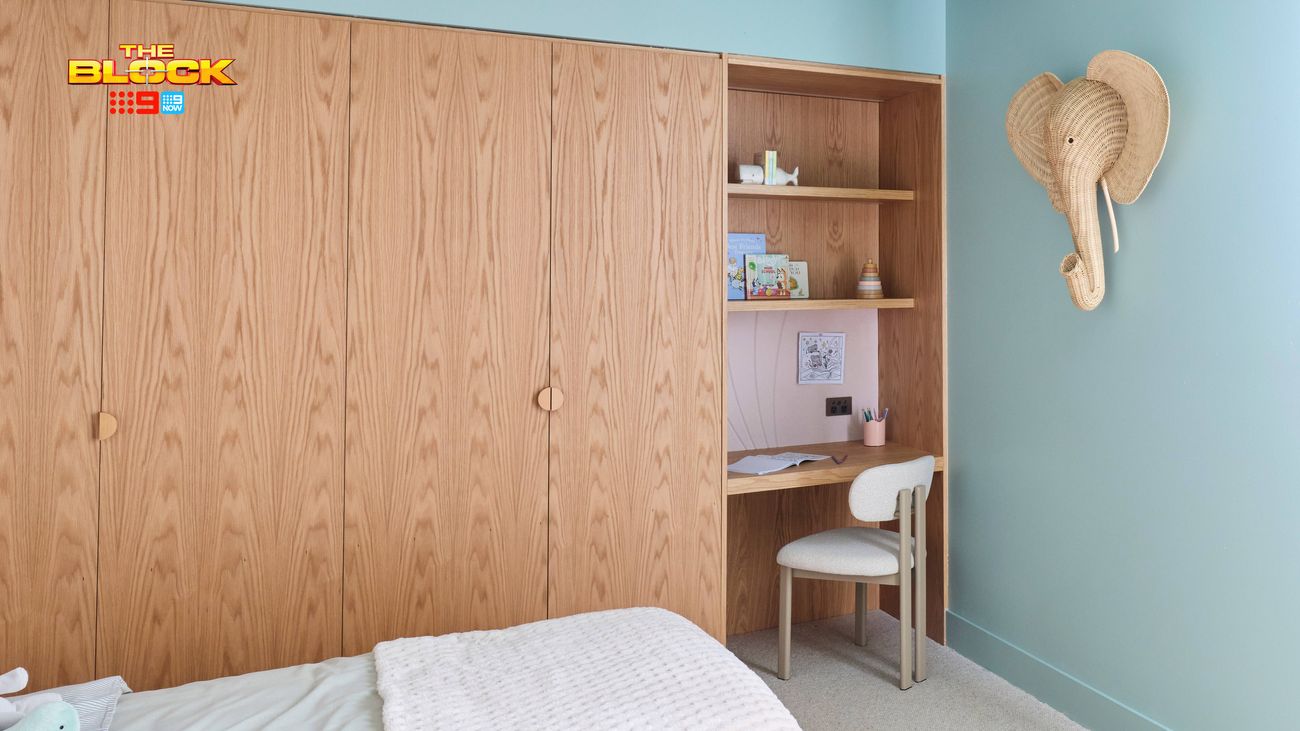 Children’s bedroom featuring built-in timber wardrobes, a study nook with open shelving and an elephant wall decoration.