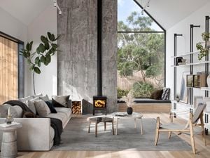 Wide shot of a living room with an indoor fire pit at the centre, with a grey couch,rug and glass coffee table in the foreground.