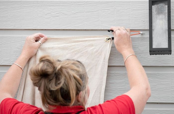 Person attaching a canvas sheet to a cup hook using shock cord