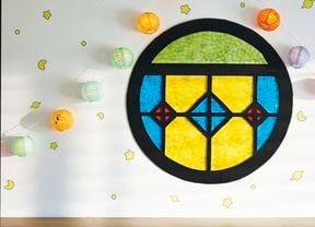 A round stained glass-look window made from black flute board with coloured cellophane as the panes, attached to a wall with paper lanterns and glow in the dark stickers