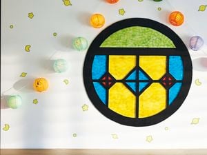 A round stained glass-look window made from black flute board with coloured cellophane as the panes, attached to a wall with paper lanterns and glow in the dark stickers