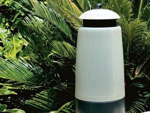An EnviroSafe outdoor white fly trap against a backdrop of palms and other greenery.