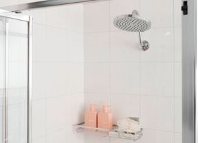 A new shower head and neatly organised shampoo and conditioner on a wall shelf.
