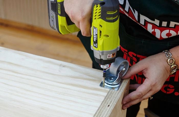 Castor wheels being secured to the bottom of a laundry basket dresser