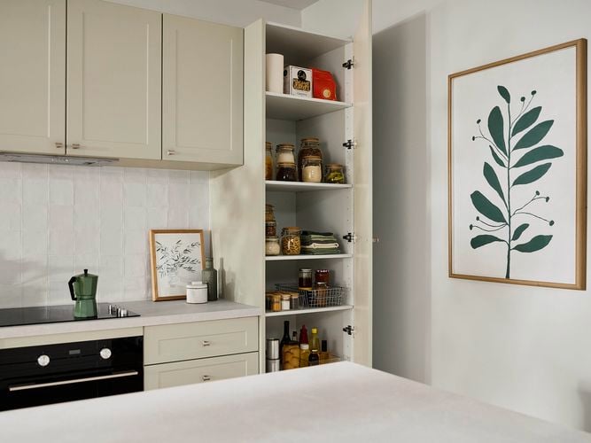 Modern Beige kitchen with a painting on the wall, a pantry, white benchtop with a stovetop and crockery on it.