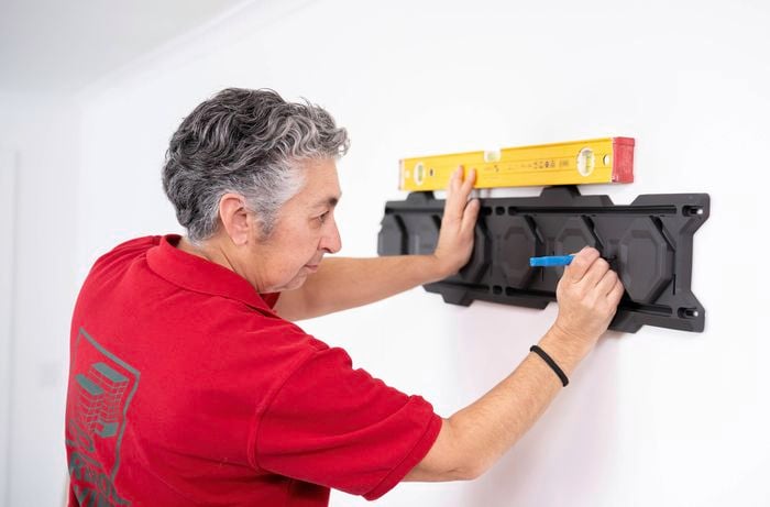 A Bunnings Team Member is using a spirit level to align a Ryobi LINK rail and marking drill points on the wall for installation