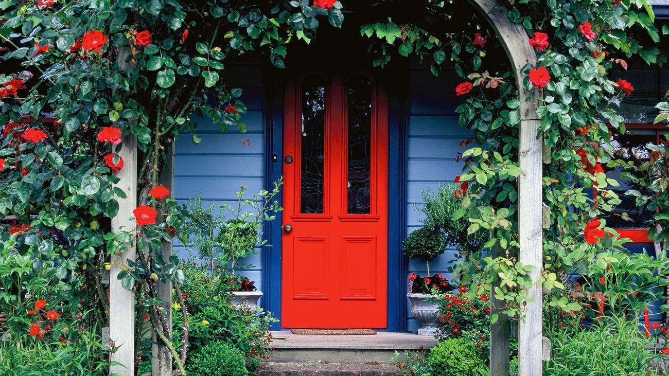 Red front door sits behind a flowered archway in a blue house