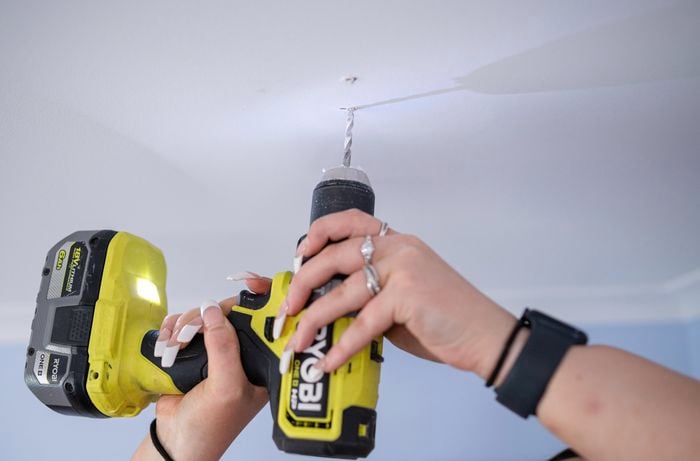 A woman drilling the ceiling using a drill.