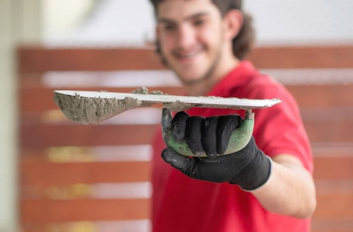 A person in a red shirt and black gloves is holding a trowel upside down with a small amount of mortar mix on it