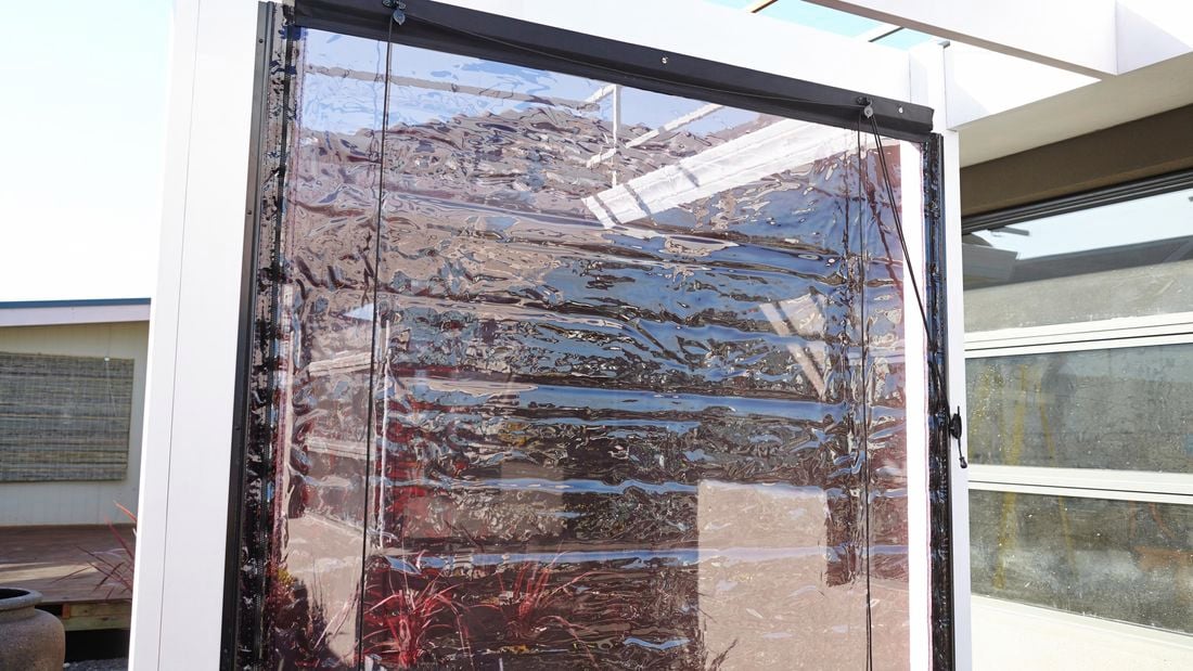 A clear bistro blind hanging from the beam of a pergola