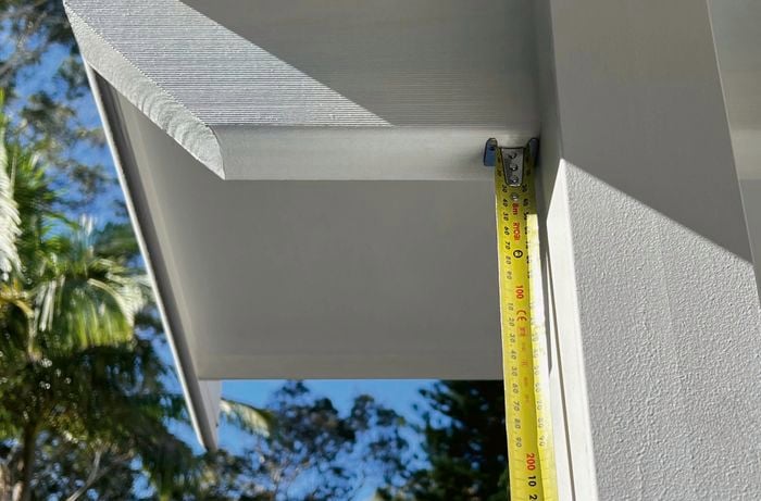 A measuring tape is put up to the roof, underneath the rafter.
