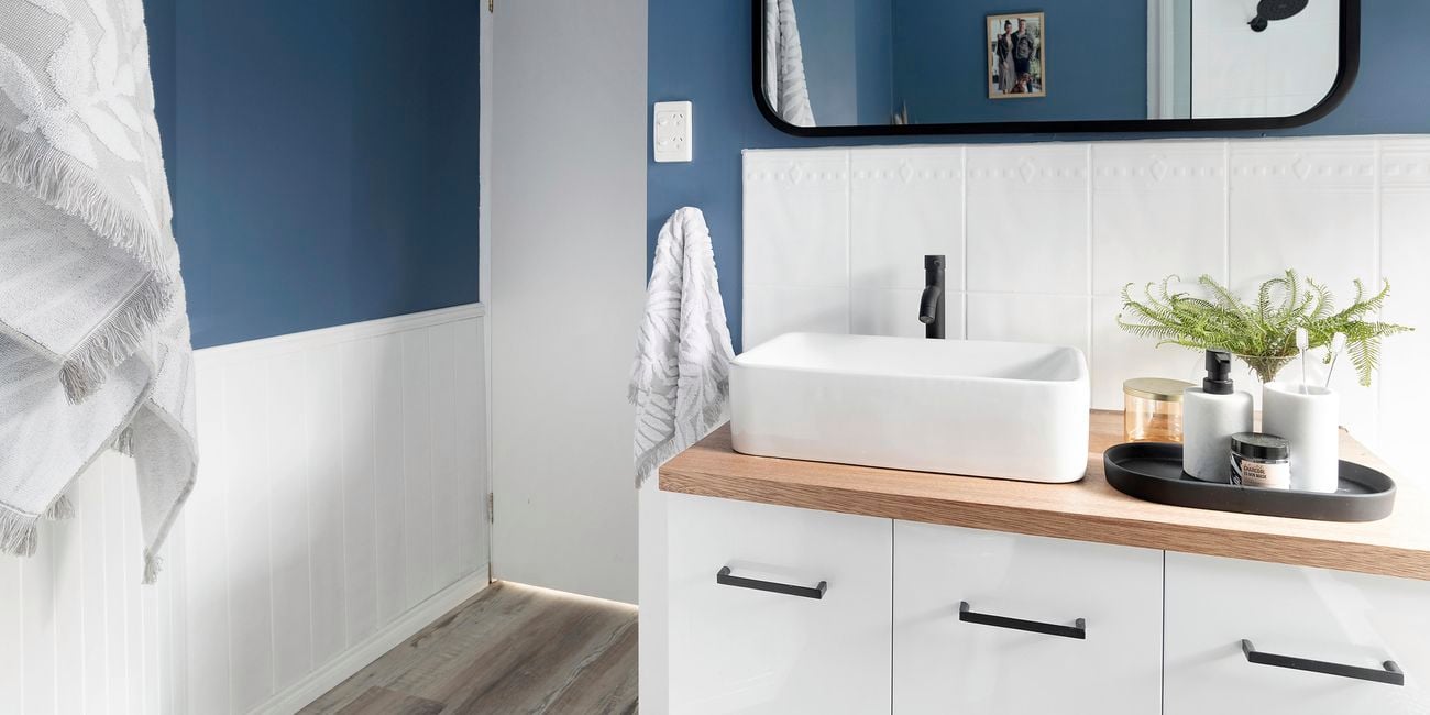 Bathroom with blue walls, white tiles, timber vanity and black mirror frame.