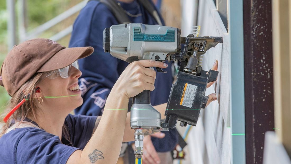 A young woman in construction using a Makita nail gun on a building site