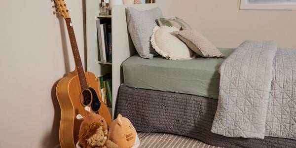 A bed in a room with a window and a guitar next to the bed.
