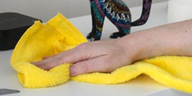 Person wiping table with yellow microfibre cloth.