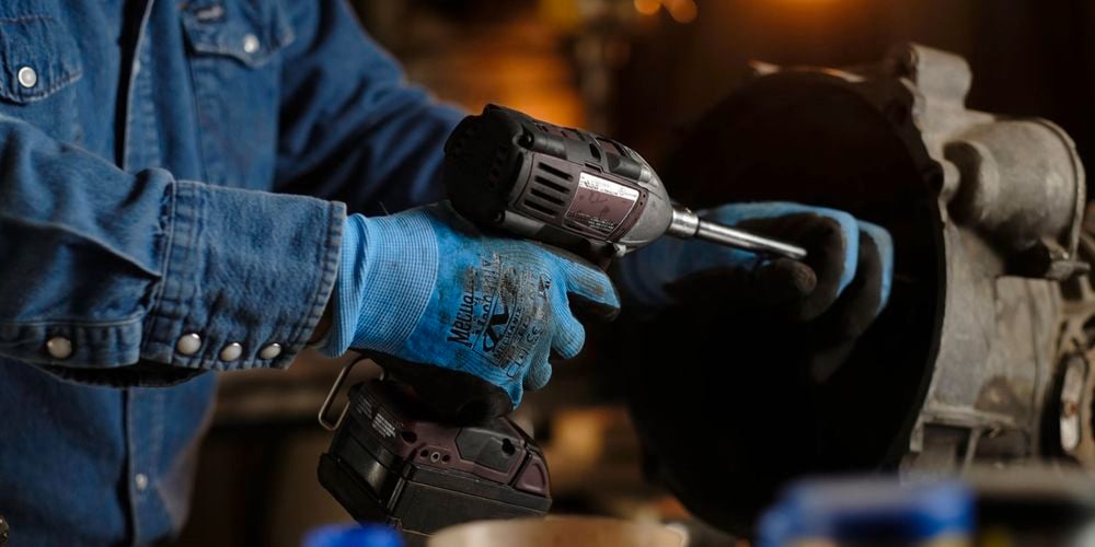 Person holding a drill and drilling whilst wearing protective gloves