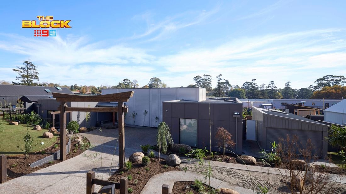 The front of a house with a driveway, trees, grassed area and rocks in it.