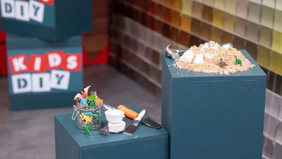 A pile of sand with toy dinosaurs and plaster fossils, accompanied by excavation tools.] 