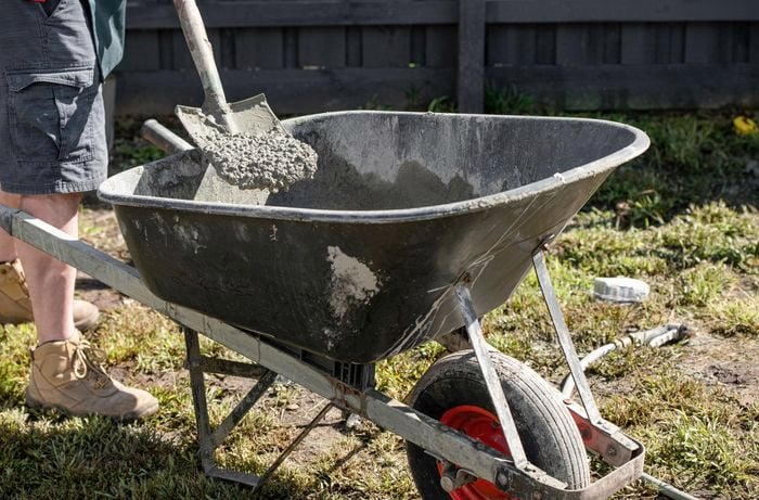 Concrete being mixed in a wheelbarrow with a shovel