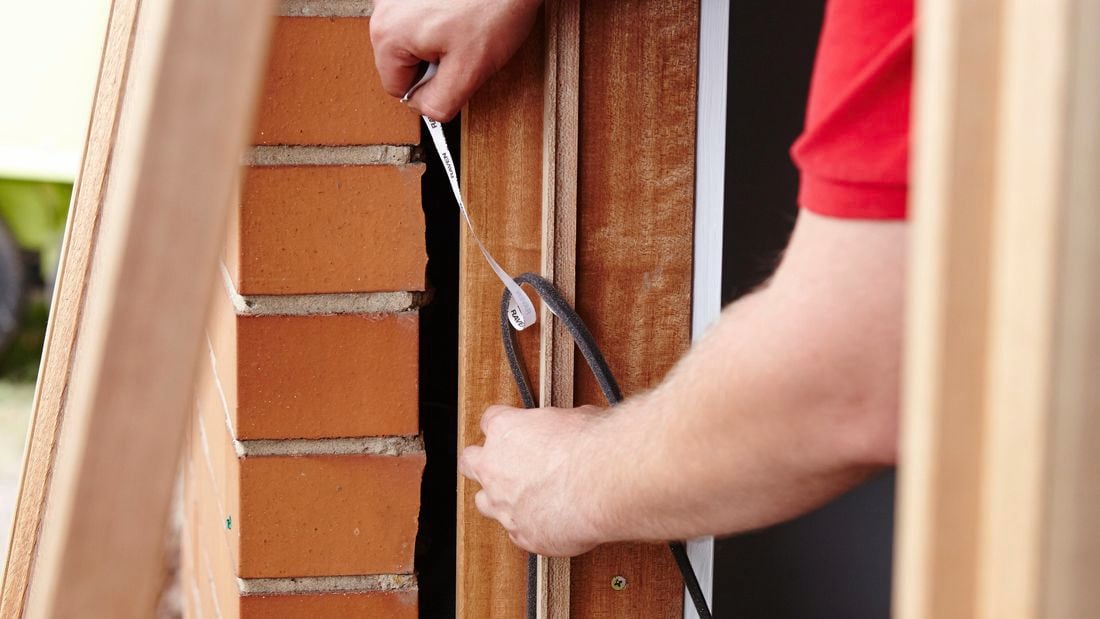 Person sticking weather strip to window frame.