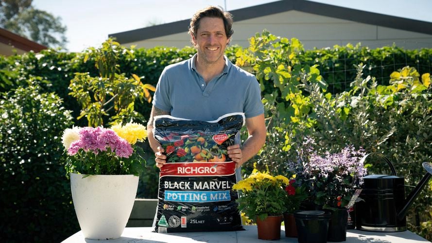 Man with potting mix bag on table with flower pots and watering can. 