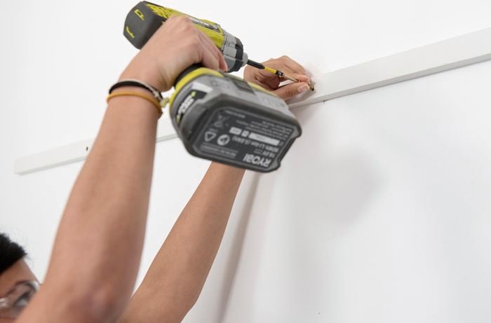 Person drilling screw into wall slat.