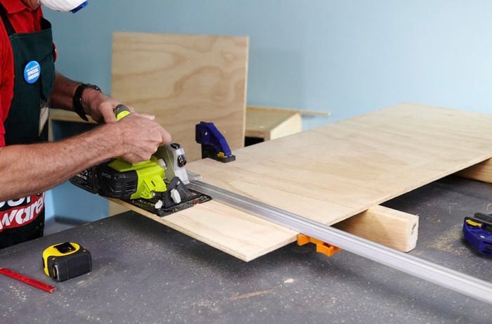 A person cutting a timber panel using a circular saw and straight edge